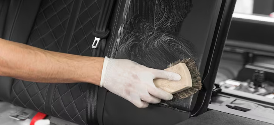 Gloved hands gently scrubbing beige leather car seat with dedicated cleaning brush