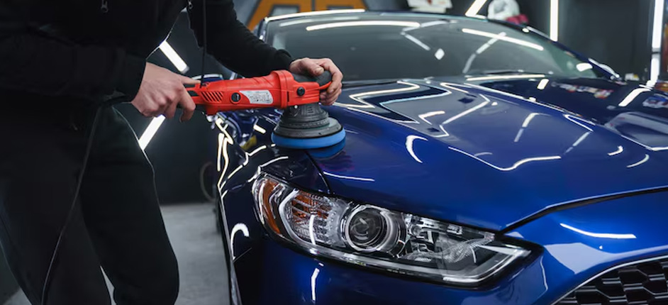 Technician using dual-action polisher on black car hood to restore glossy finish