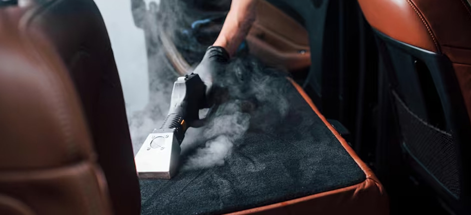 Steam cleaning nozzle treating stained fabric seats inside a compact car interior
