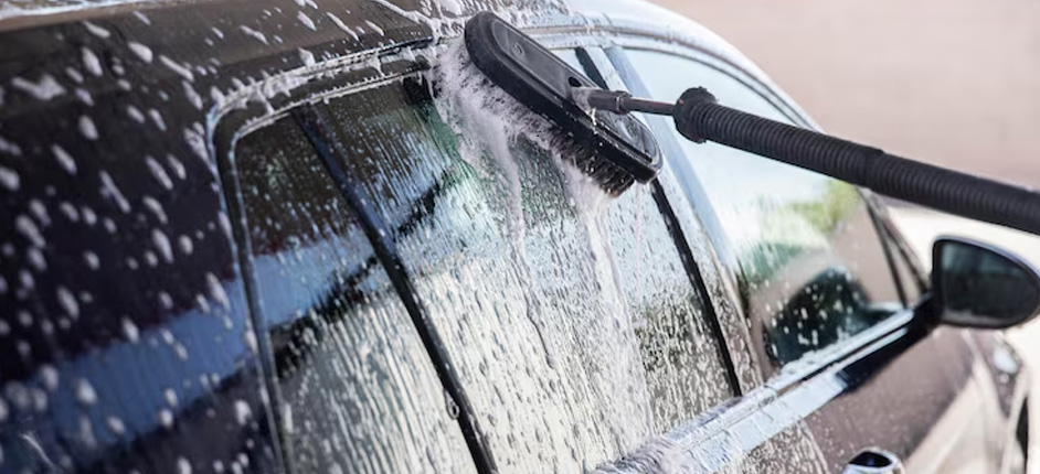 Detailing technician wiping down a parked sedan near Washington DC rowhouses
