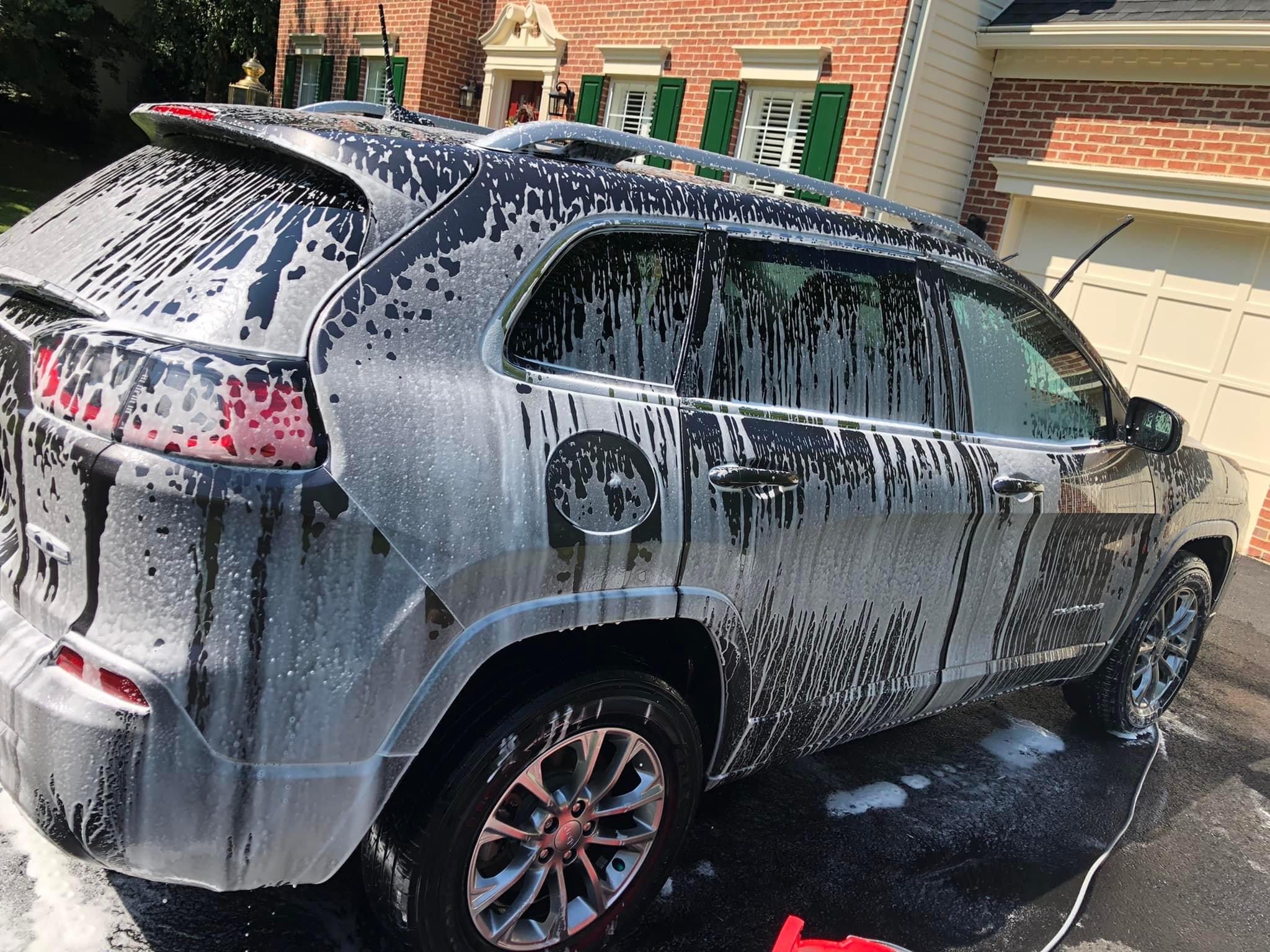 Detailer covering a dark SUV in thick foam during Alexandria driveway wash